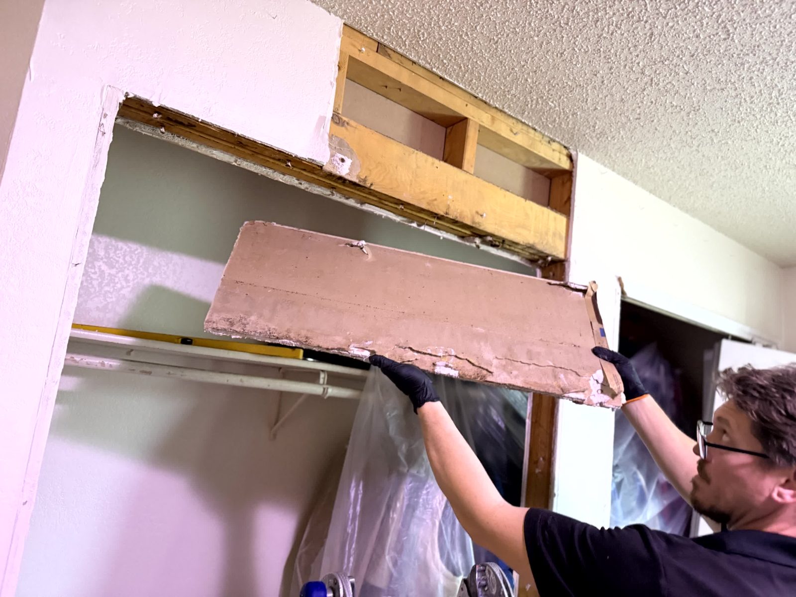 Technician removing water-damaged wallboard above a doorway