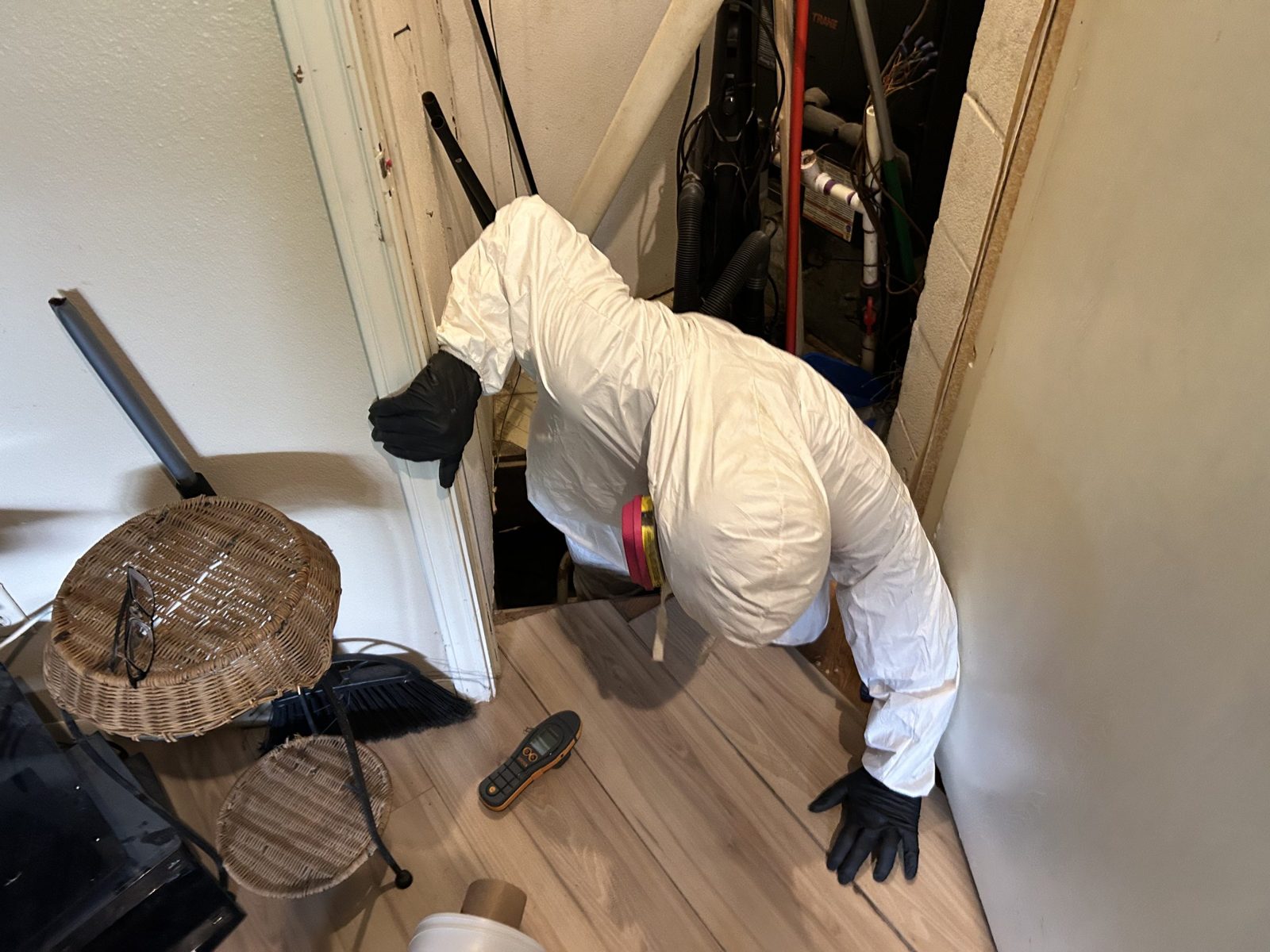 Technician in full protective gear entering a crawlspace hatch